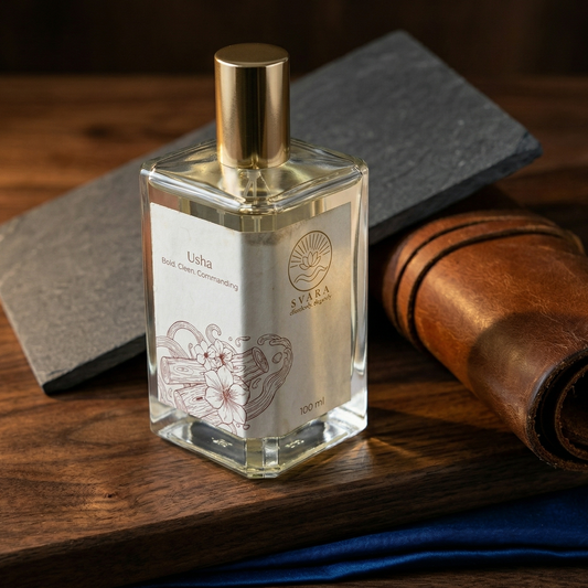 A bottle of Svara Usha wellness perfume on a dark wood surface, styled with slate and leather textures to represent a bold and commanding fragrance profile.