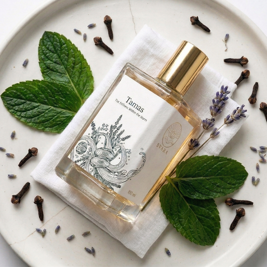 A flat lay of Svara Tamas magnesium oil perfume bottle on a white plate, surrounded by fresh mint leaves, dried lavender buds, and cloves.